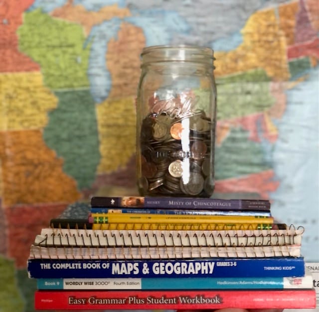 Glass jar of coins, on a stack of homeschool workbooks, in front of a map