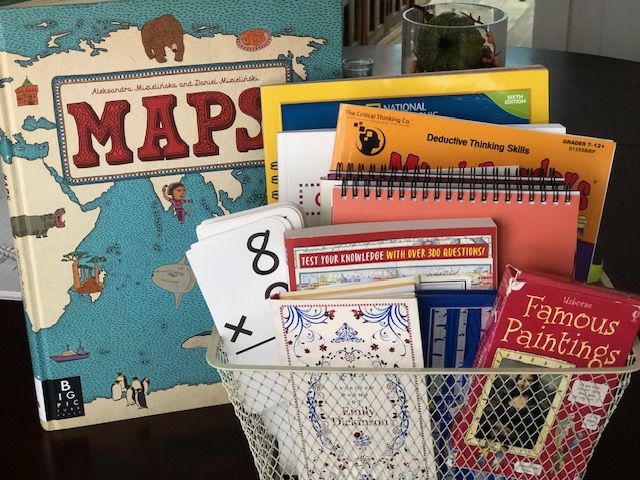 Maps book next to basket with books and flashcards for homeschool