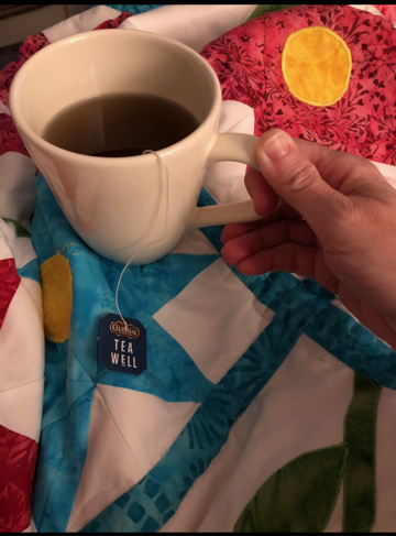 cup of tea being held over a colorful quilt as part of dealing with homeschool burnout