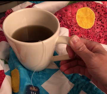 cup of tea being held over a colorful quilt as part of dealing with homeschool burnout